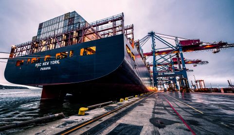 Large container ship docked at a port with cranes in the background
